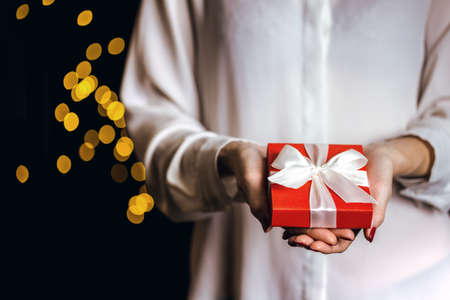 girl holding beautiful  gift for the day valentines day. red box and white bow and bokeh in the background
の写真素材