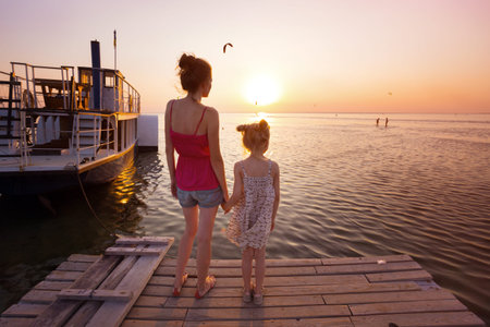 family - mother and daughter standing on the pier in sunset lightの写真素材