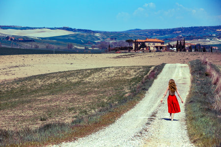 girl is walking along the road among the fields and a typical Tuscan landscape behind her. Tuscany, Italyの写真素材