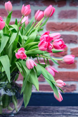 beautiful pink tulips in a vase against a brick wall backgroundの写真素材
