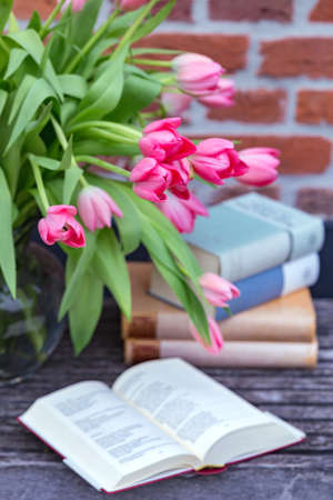 beautiful pink tulips in a vase and books against a brick wall backgroundの写真素材