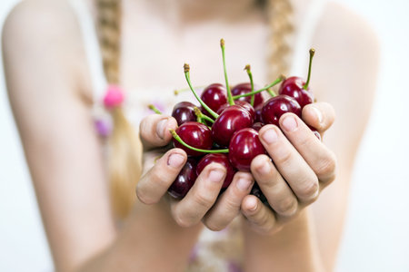 summer - the girl is holding a ripe red cherry in her handsの写真素材