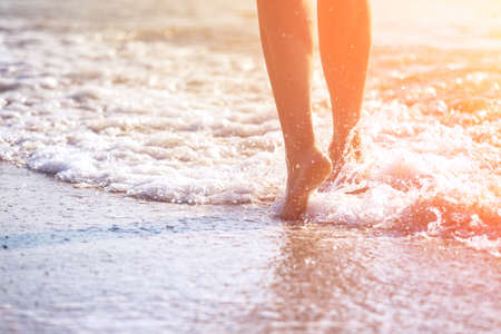 close up leg of young woman walking along wave of sea water and sand on the summer beach. Travel Concept.の写真素材