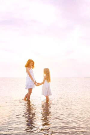 happy weekend by the sea - Mom and daughter in white dresses walking by the sea at sunset. Ukrainian landscape at the Sea of Azov, Ukraineの写真素材