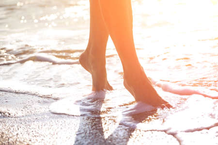 close up leg of young woman walking along wave of sea water and sand on the summer beach. Travel Concept.の写真素材