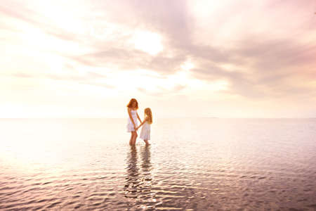 happy weekend by the sea - Mom and daughter in white dresses walking by the sea at sunset. Ukrainian landscape at the Sea of Azov, Ukraineの写真素材