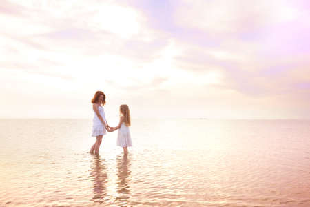 happy weekend by the sea - Mom and daughter in white dresses walking by the sea at sunset. Ukrainian landscape at the Sea of Azov, Ukraineの写真素材