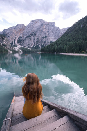 autumn - girl sits on the pier and view of well-known tyrolean lake lago di Braies Dolomites Italy
