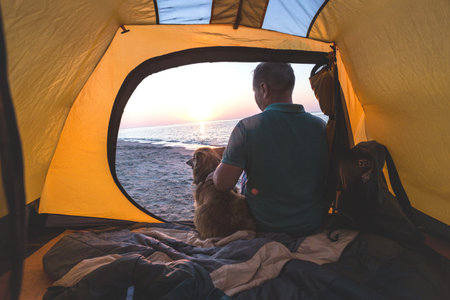 happy weekend by the sea - man with a dog in a tent on the beach at dawn. Ukrainian landscape at the...