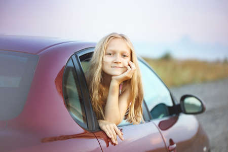 happy smiling little girl looking out the car window and sunset at the backgroundの写真素材