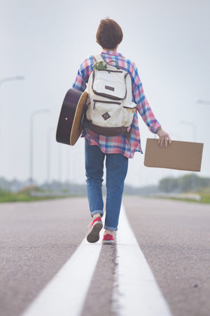Young girl with a guitar coming along the road and hitch-hiking