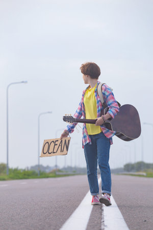 Young girl with a guitar coming along the road and hitch-hiking