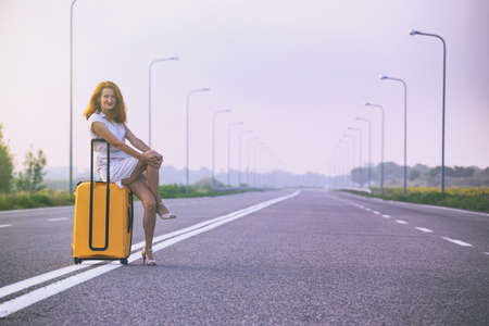 problems in the journey. the girl is sitting on a yellow suitcase on the side of the roadの写真素材