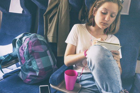 Stylish teenage girl is going by train. Draws and listens to music