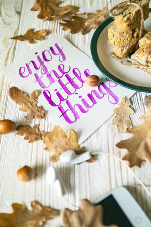 Beautiful autumn background - cup of tea, biscotti, autumn leaves and sheet with a quote