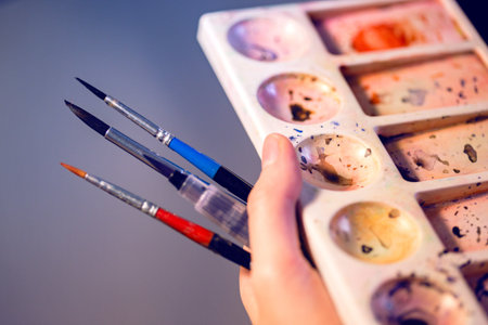 girl holds in her hand brush and watercolor palette