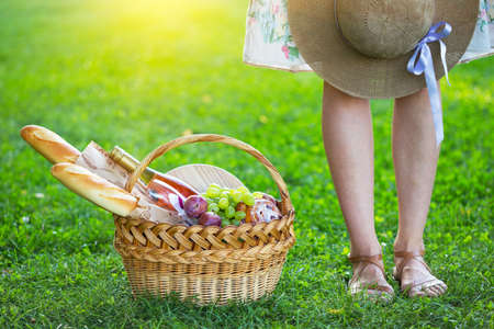 Summer - picnic on the lawn in the park.   girl and basket for a picnic with baguette, wine, glasses, grapes and rollsの写真素材