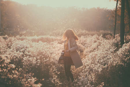 vintage autumn. girl with a vintage camera walks in the fields of fluffy dandelions at sunsetの写真素材