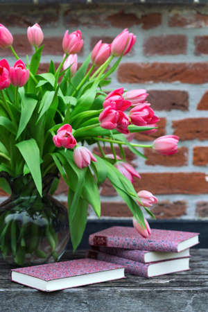 beautiful pink tulips in a vase and books against a brick wall backgroundの写真素材