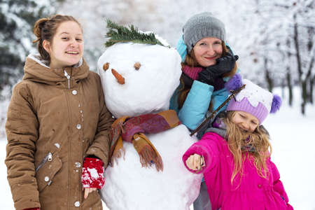 happy family - smiling mother and daughters with snowman at the winter dayの写真素材