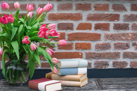 beautiful pink tulips in a vase and books against a brick wall backgroundの写真素材