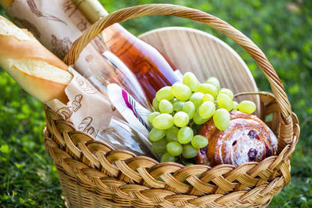 Summer - picnic in the meadow.  baguette, wine, glasses, grapes and rolls in a basket on green grassの写真素材