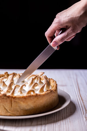 famous french dessert - delicious lemon tarts and classic meringue topping. girl cuts cake with...