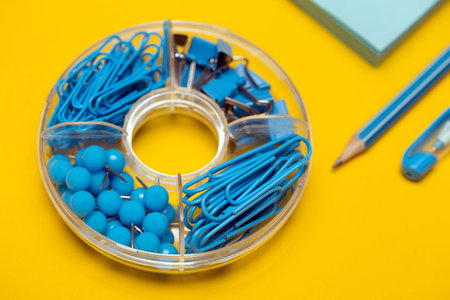 stationery paper clips, binders, buttons, pencil, pen and paper in blue on yellow background