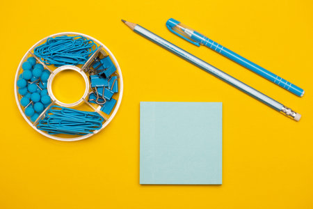 stationery paper clips, binders, buttons, pencil, pen and paper in blue on yellow background