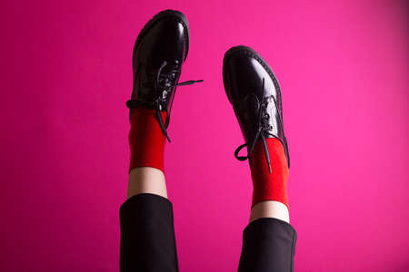 female legs in red socks and stylish black shoes on a pink background. fashion trends. beautiful female shoesの写真素材
