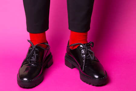 female legs in red socks and stylish black shoes on a pink background. fashion trends. beautiful female shoesの写真素材