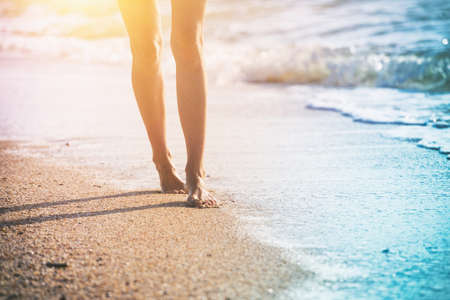 close up leg of young woman walking along wave of sea water and sand on the summer beach. Travel Concept.の写真素材