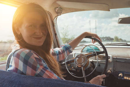 young girl driving a retro car by the road at the fieldsの写真素材