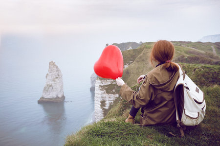 happy girl with a red balloon in the shape of a heart at background of scenery Etretat. France