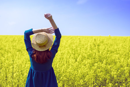 Happy girl in a hat walking in amazing field of yellow rapeseed in the countryside. Emotions