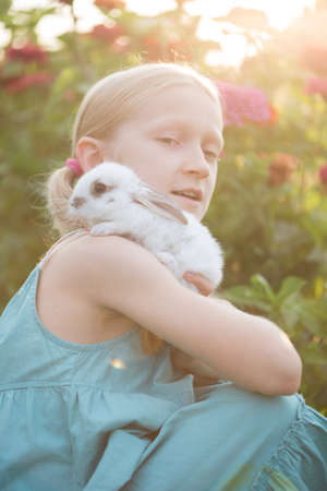 beautiful little girl holding in hands white rabbit at the gardenの写真素材