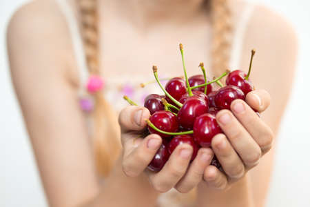 summer - the girl is holding a ripe red cherry in her handsの写真素材