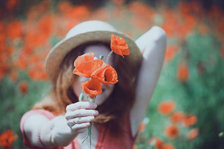 Happy girl in a hat  at the amazing field of beautiful red poppy field  in the countryside.の写真素材
