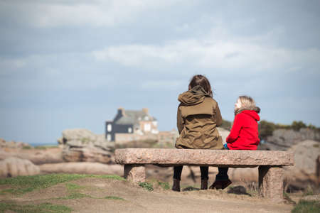 the sisters are sitting on a bench near the sea and the shore at  the Tregastel, Brittany. Franceの写真素材