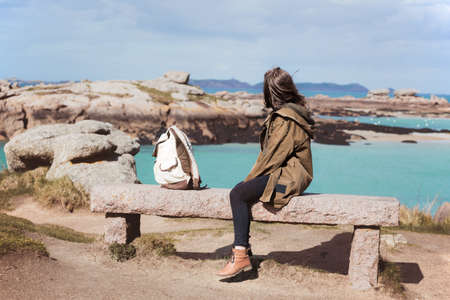 girl traveler sits on a bench near the sea and the shore at  the Tregastel, Brittany. Franceの写真素材