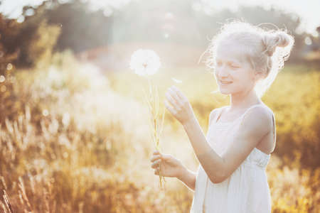 blonde Little girl holding dandelion and blowing it on the Sunset. summer holidays and moodの写真素材