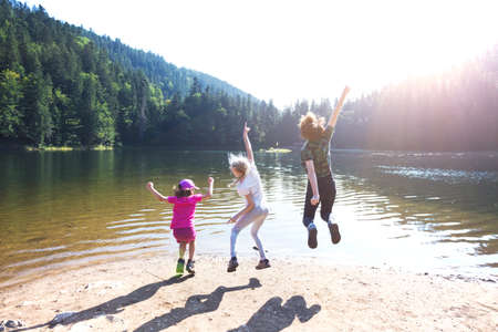 Summer - three sisters on a hike. Fun happy family  jumping on the shore of a mountain lake synevyr.の写真素材