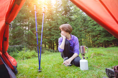hike and camping life. view from the tent on tourist girl cooks food on a burnerの写真素材