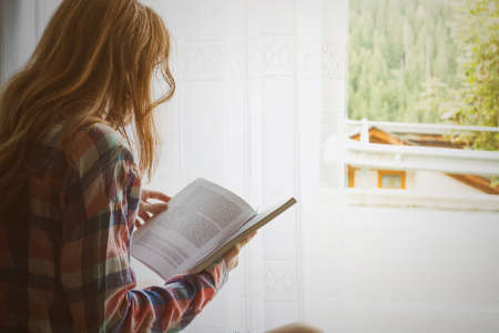 girl holding a book sitting on a windowsill with bright sun light from the windowの写真素材