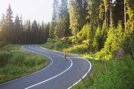 Summer Road Trip. beautiful landscape and view of a mountain road. girl rides on a skateboard at the transalpine. Romania.の写真素材