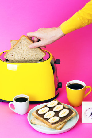 bright, fun breakfast. girl preparing toasts. yellow toaster and a cup of coffee on a pink...