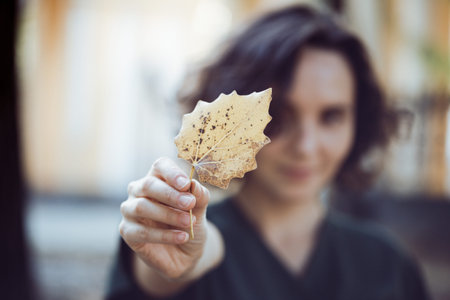 autumn mood - fun happy girl holds a yellow leaf. focus on the sheet