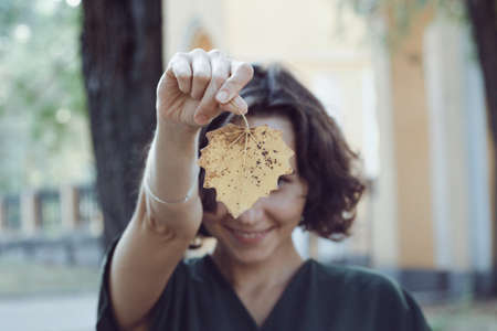 autumn mood - fun happy girl holds a yellow leaf. focus on the sheetの写真素材