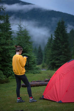 red tent  in the evening pine forest and girl near. clouds in the backgroundの写真素材
