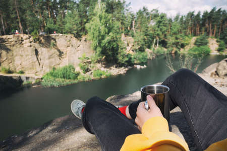 girl hiker sitting by the lake and  holding a cupの写真素材